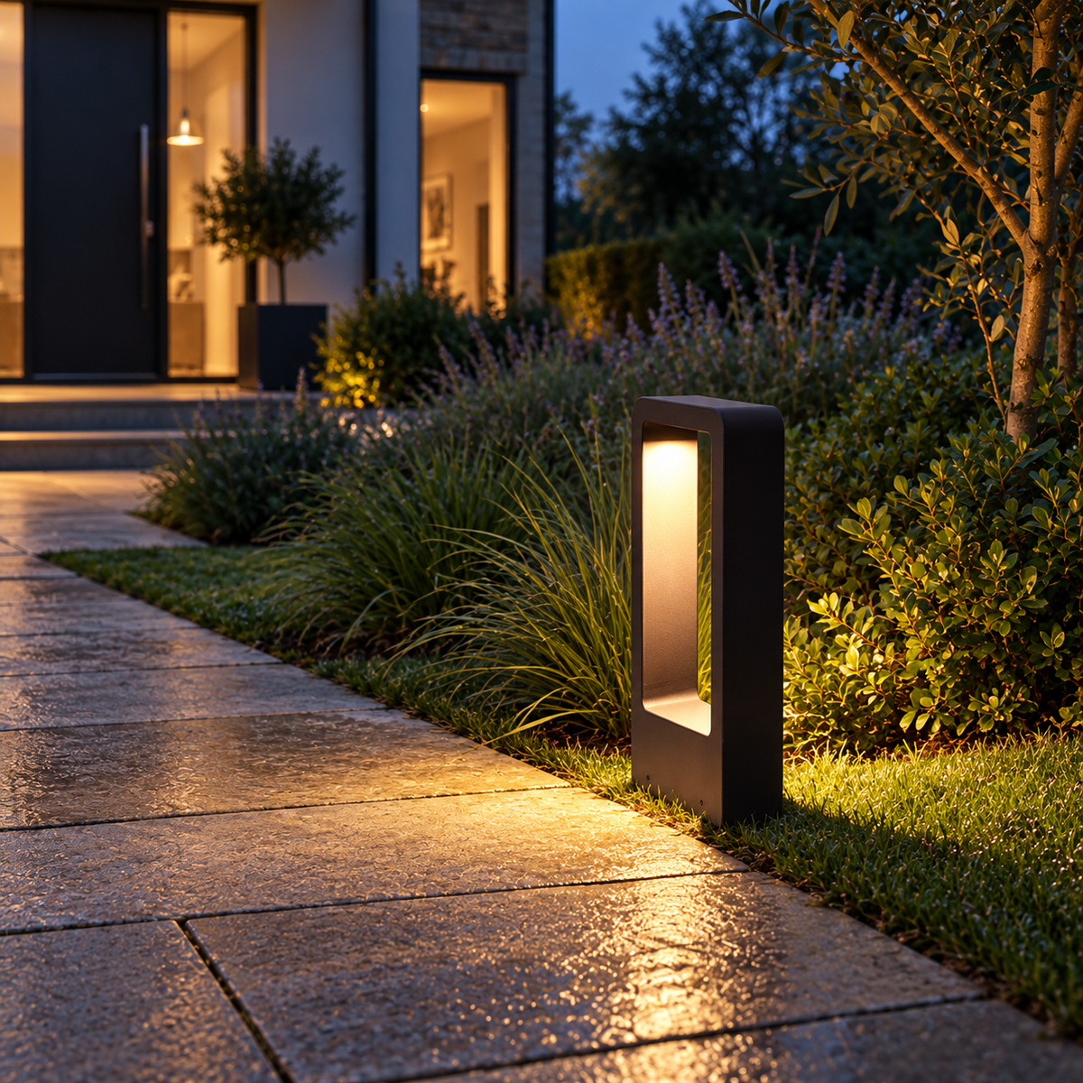 Black 30cm LED garden bollard light illuminating a stone path at dusk